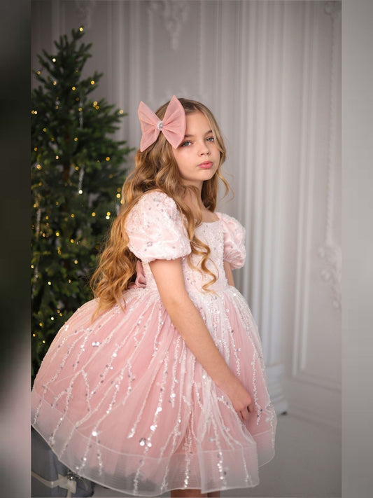 a little girl in a pink dress standing in front of a christmas tree