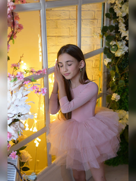 a young girl in a pink dress standing in front of a window