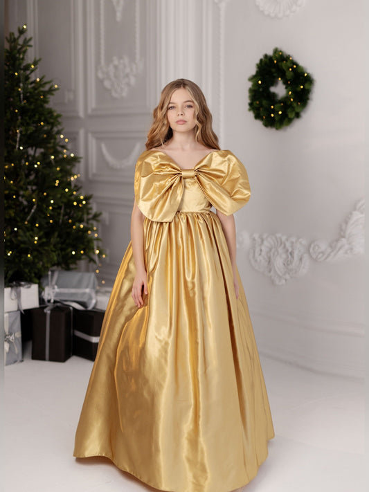 a woman in a gold dress standing in front of a christmas tree