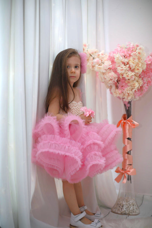 Delicate pink ruffle dress made of cotton, tulle, satin, and adorned with pearls, perfect for special occasions.