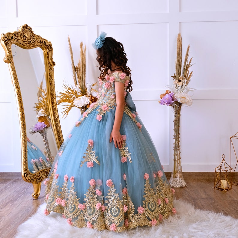 The bodice of the light pastel blue dress is laced and has laser flowers on it. The whole skirt is embroidered with lace and tulle on tulle. Baby Girl Dress