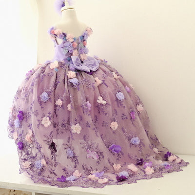 Stunning lilac quinceañera dress with a satin bodice embellished with delicate lace and 3D floral accents, complemented by a full tulle skirt with sparkling details and a matching hair accessory, ideal for a special celebration.