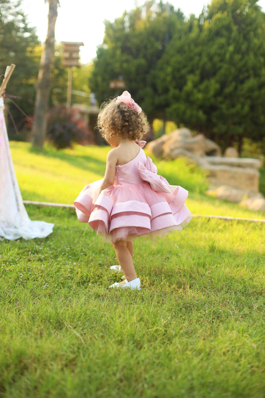 Blush pink one-shoulder dress for girls, showcasing a chic and modern design with a single strap and a flared skirt. Ideal for formal events, this dress adds a touch of sophistication and charm to any young girl's wardrobe.