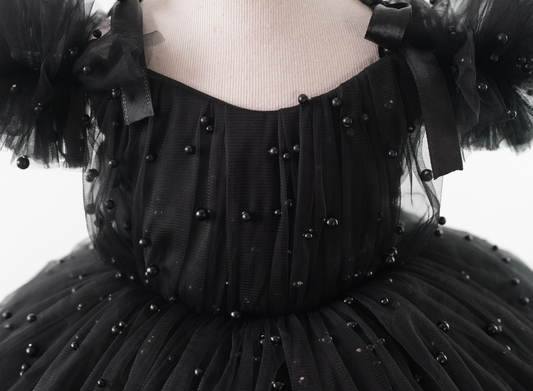 a woman wearing a black dress with pearls on it