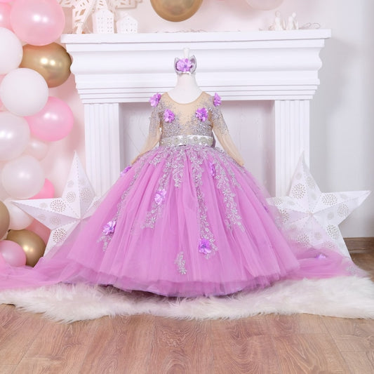 Lilac quinceañera dress featuring a satin bodice with intricate lace and 3D floral accents, a layered tulle skirt with sparkling glitter, and a matching hair accessory, perfect for a special celebration.