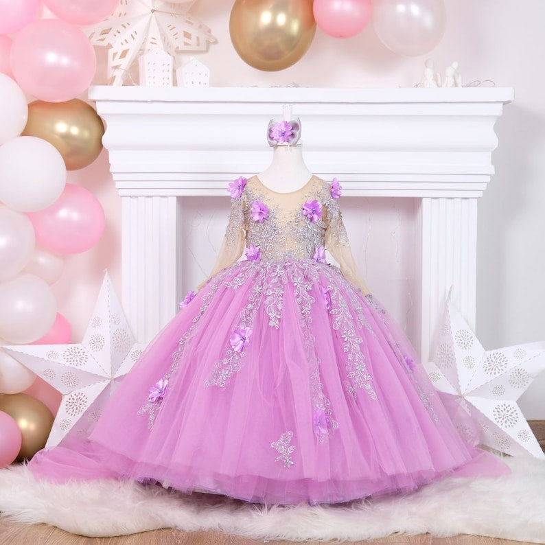 Elegant lilac quinceañera dress with a satin bodice embellished with lace and 3D flowers, a voluminous tulle skirt with glittering details, and a coordinating hair accessory, ideal for a memorable event. Baby Girl Dress