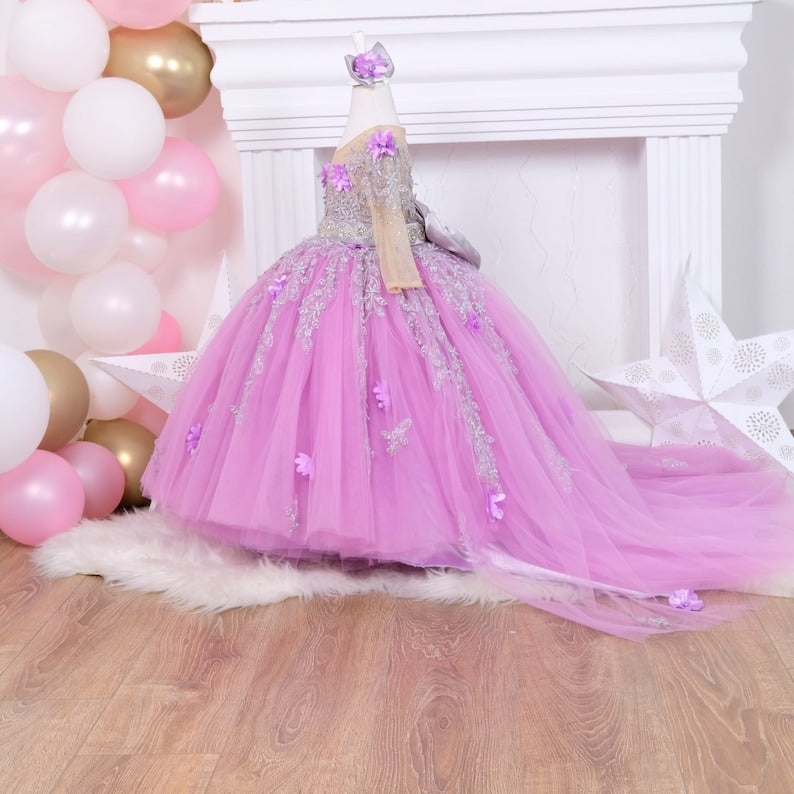 Elegant lilac quinceañera dress with a satin bodice embellished with lace and 3D flowers, a voluminous tulle skirt with glittering details, and a coordinating hair accessory, ideal for a memorable event. Baby Girl Dress