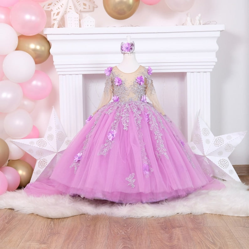 Charming lilac quinceañera dress with a satin bodice detailed with lace and colorful 3D flowers, a full tulle skirt adorned with glitter, and a matching hair accessory, designed for a stunning celebration. Baby Girl Dress