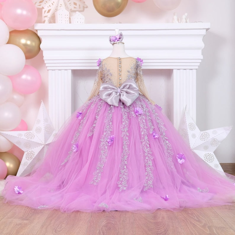 Charming lilac quinceañera dress with a satin bodice detailed with lace and colorful 3D flowers, a full tulle skirt adorned with glitter, and a matching hair accessory, designed for a stunning celebration. Baby Girl Dress