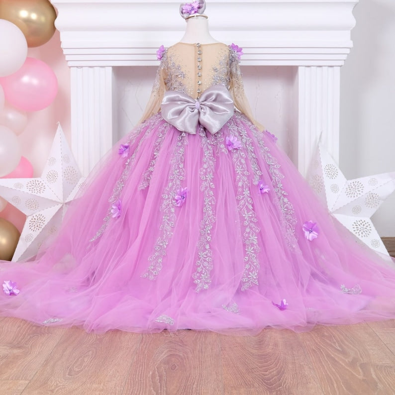 Charming lilac quinceañera dress with a satin bodice detailed with lace and colorful 3D flowers, a full tulle skirt adorned with glitter, and a matching hair accessory, designed for a stunning celebration. Baby Girl Dress