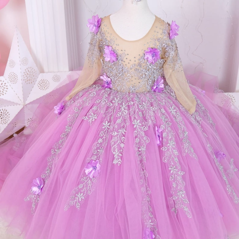 Charming lilac quinceañera dress with a satin bodice detailed with lace and colorful 3D flowers, a full tulle skirt adorned with glitter, and a matching hair accessory, designed for a stunning celebration. Baby Girl Dress