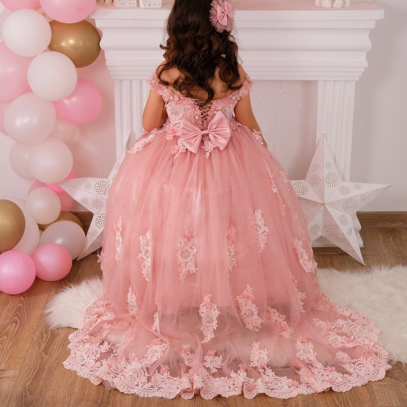 Blush quinceañera dress featuring a satin bodice with intricate lace and 3D floral details, a layered tulle skirt with glitter accents, and a matching hair accessory, designed for an elegant celebration. Baby Girl Dress