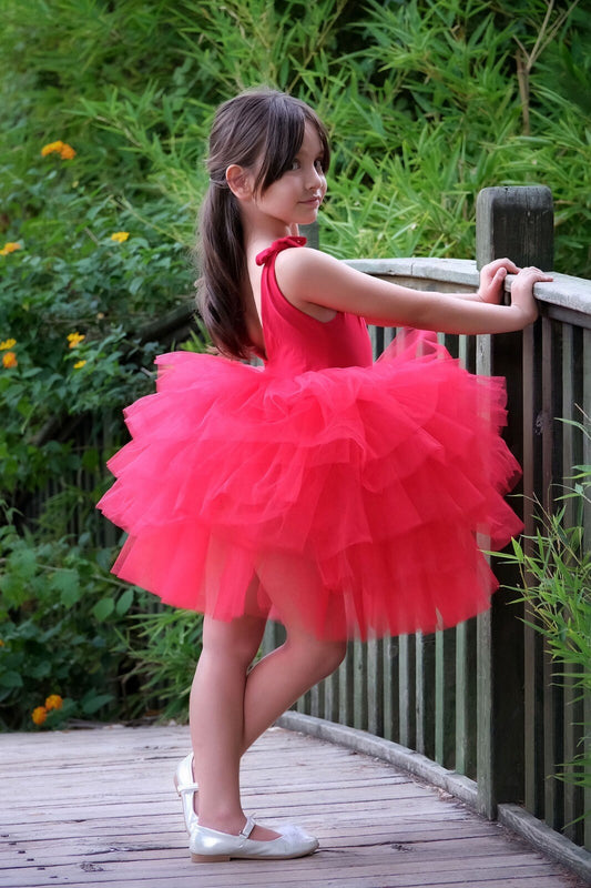 a little girl in a red dress leaning against a rail