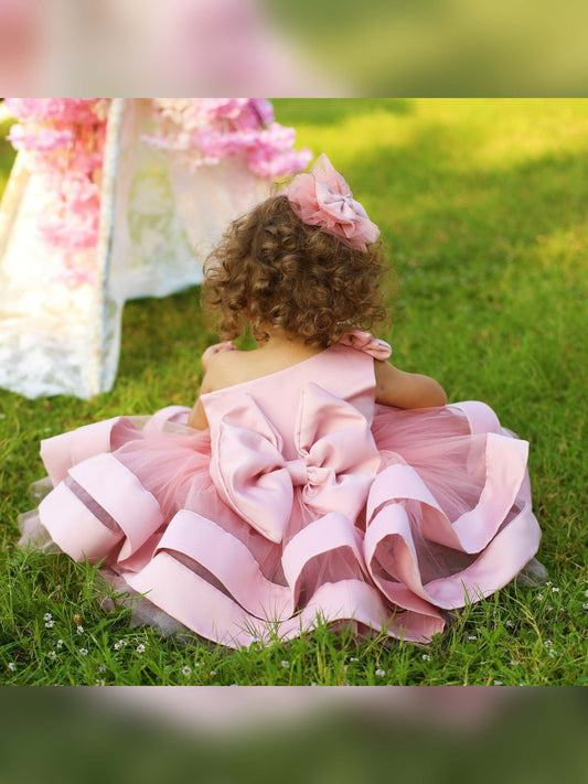 One shoulder blush pink girl’s dress featuring a stylish asymmetric design with a delicate ruffle trim, perfect for special occasions. The dress is made of soft, lightweight fabric, providing comfort and elegance for any young girl.