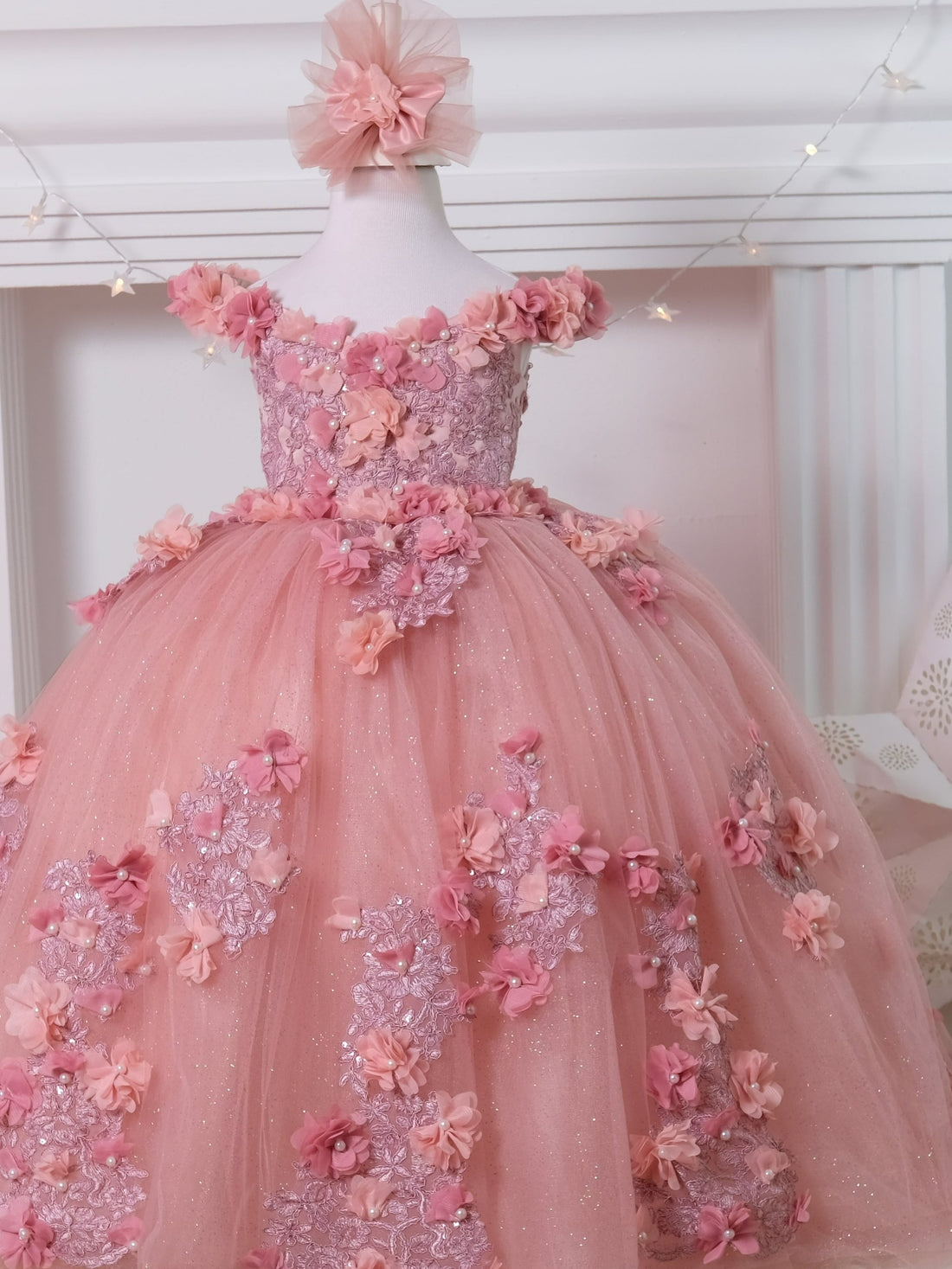 Blush pink Quinceañera gown featuring a satin bodice adorned with 3D colorful flowers and intricate lace details, with a soft cotton lining for comfort. The multi-layered tulle skirt includes glittery tulle, lace, and 3D flowers, complemented by a cotton lining. Comes with a matching gift hair accessory.