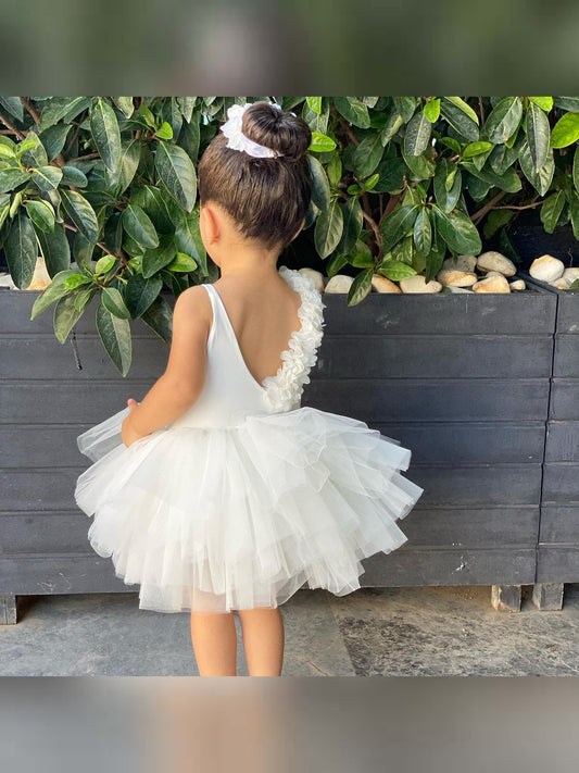 a little girl in a white dress standing in front of a plant
