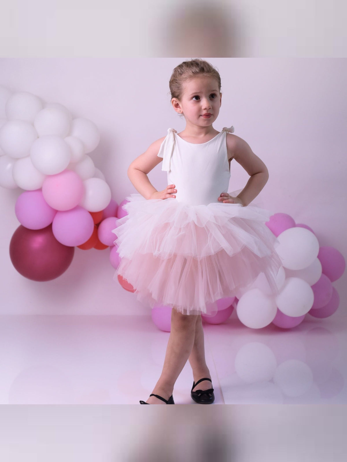 a little girl in a white dress standing in front of balloons