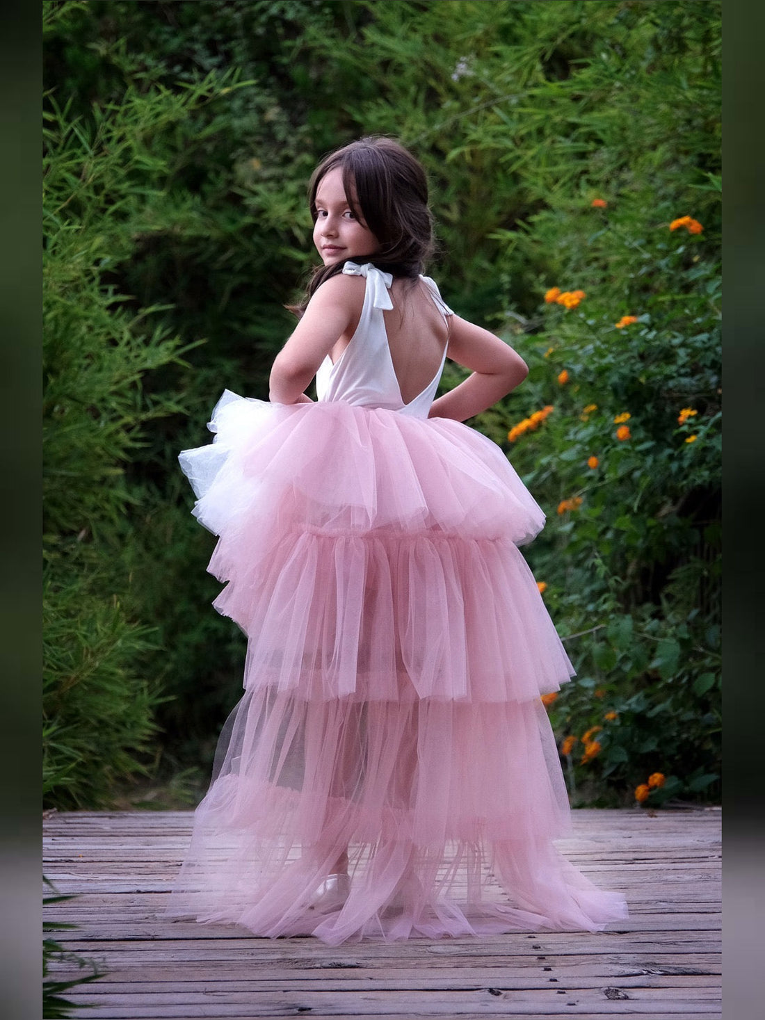 a little girl in a pink dress standing on a wooden walkway