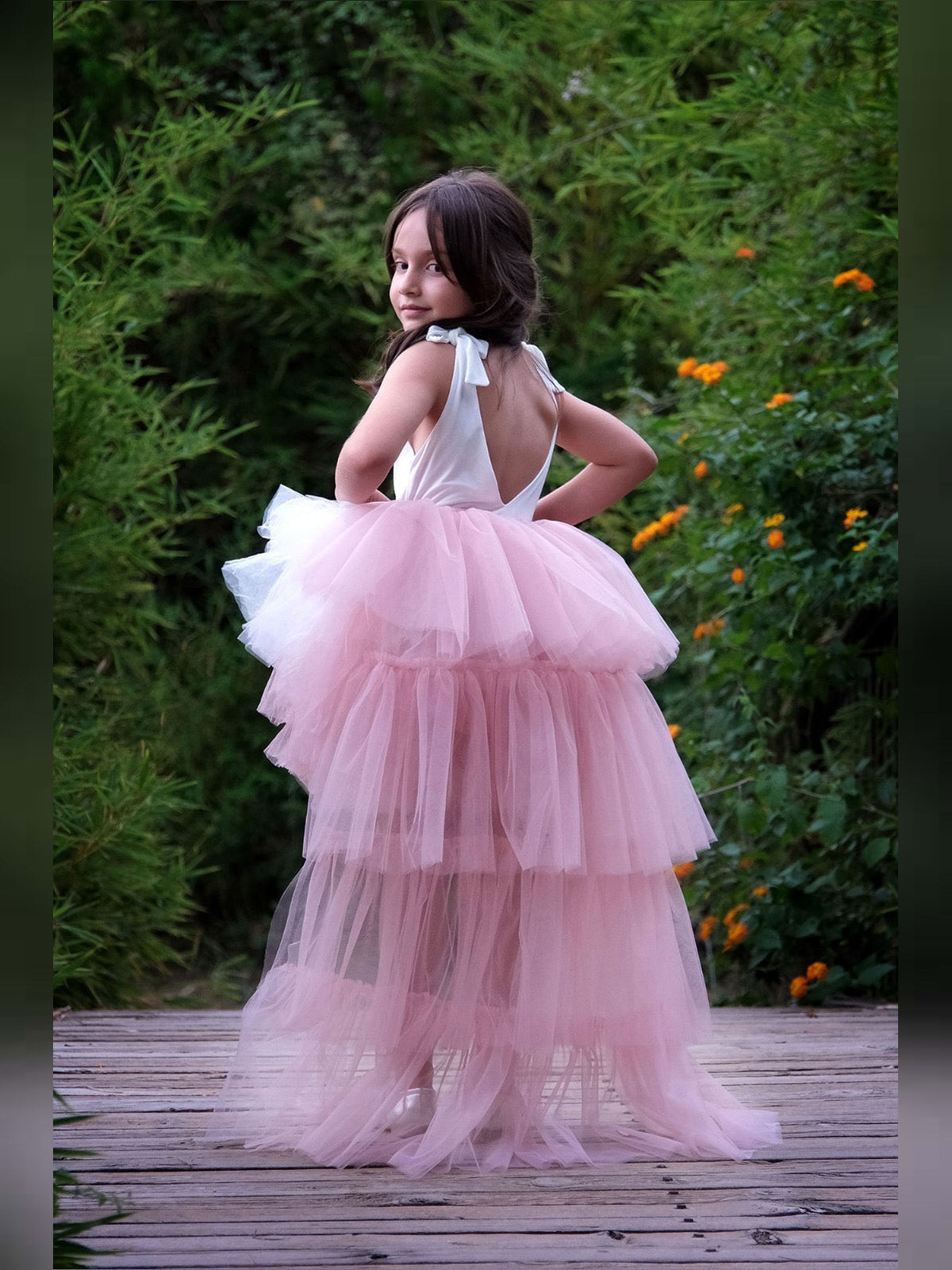 a little girl in a pink dress standing on a wooden walkway