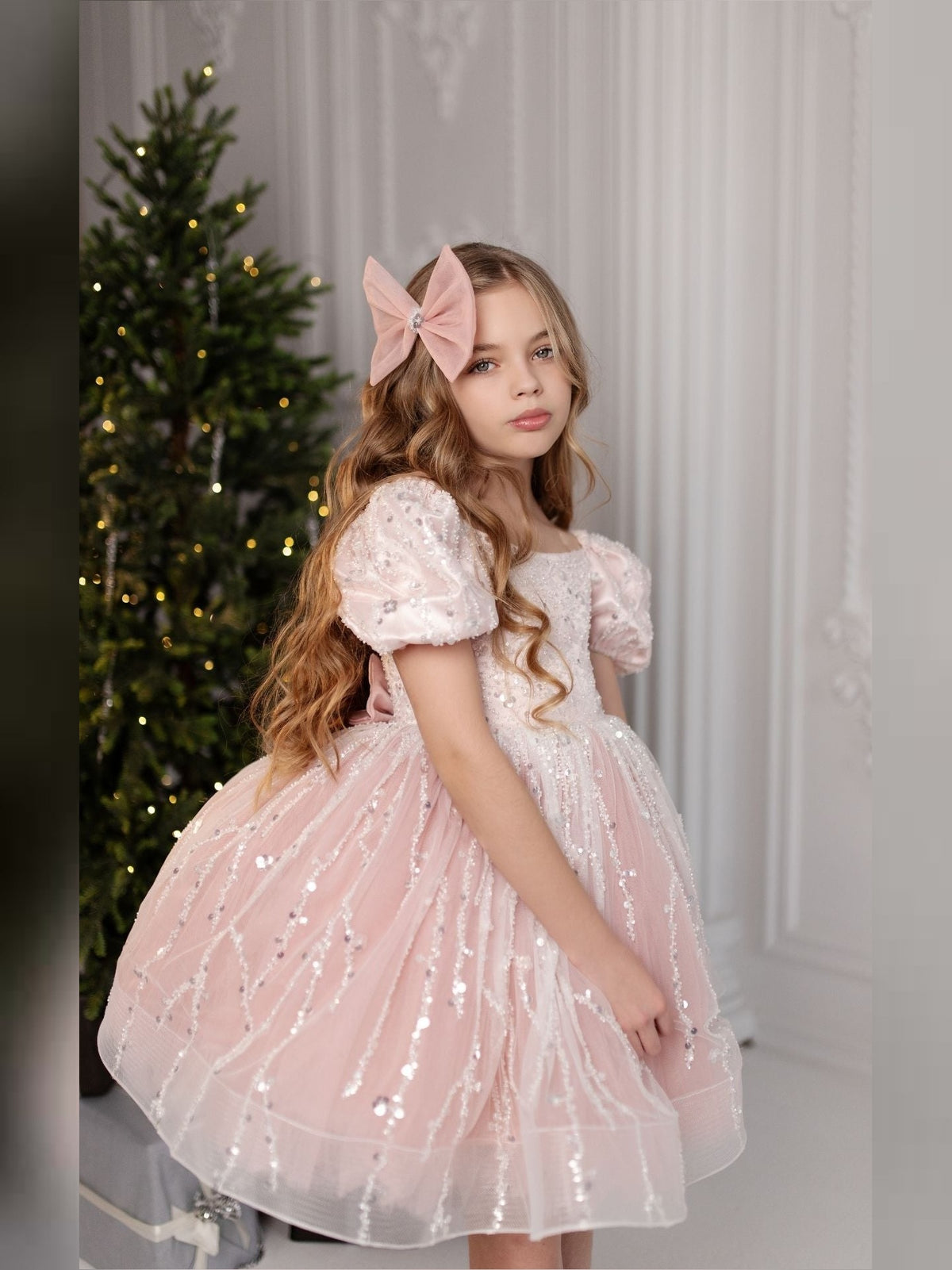 a little girl in a pink dress standing next to a christmas tree