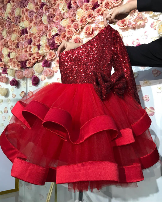  Back view of mini red baby girl Christmas dress with one shoulder and sparkling sequin details