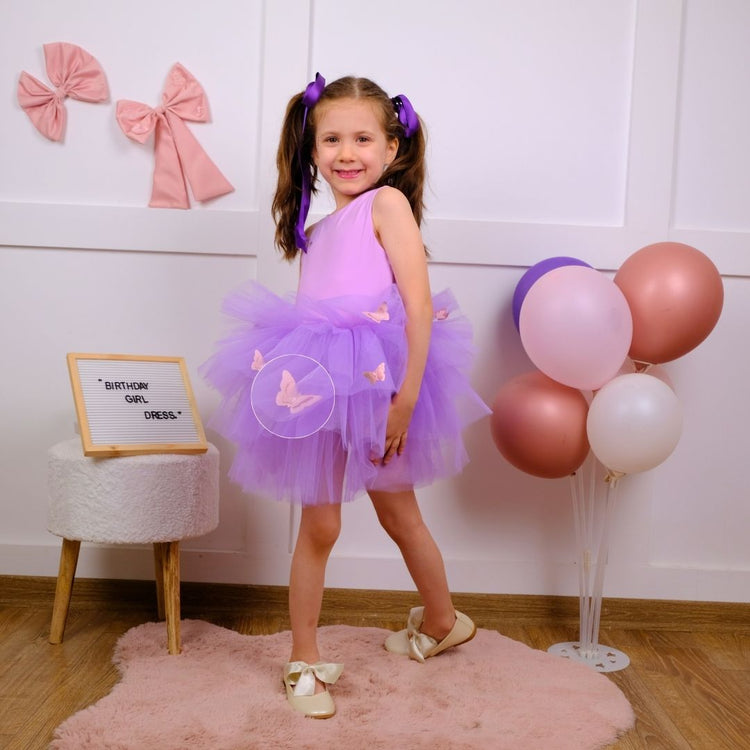 a little girl in a purple dress standing in front of balloons