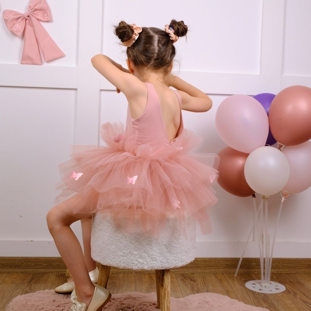 a little girl in a pink dress sitting on a stool