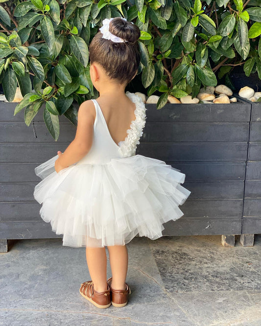 a little girl in a white dress standing in front of a plant