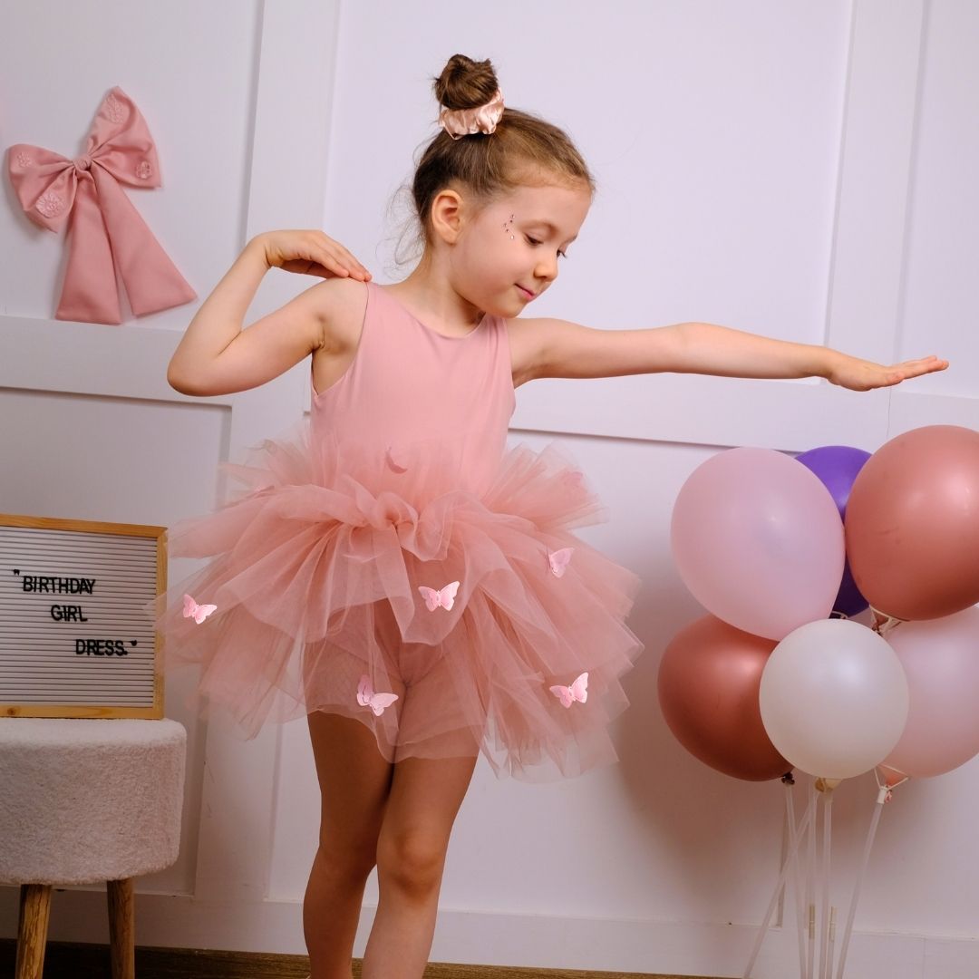 a little girl in a pink dress standing in front of balloons