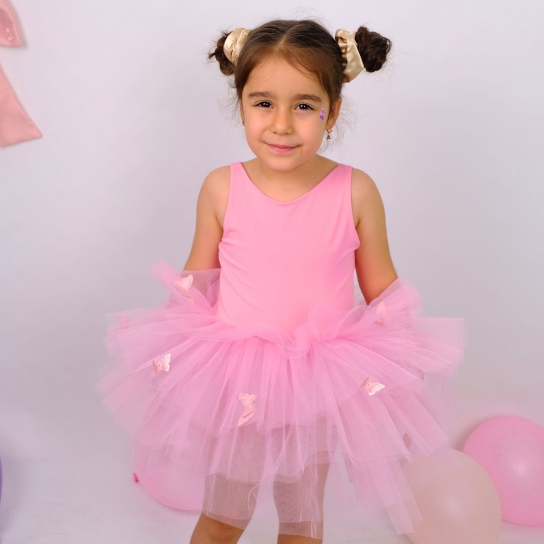 a little girl in a pink dress standing in front of balloons