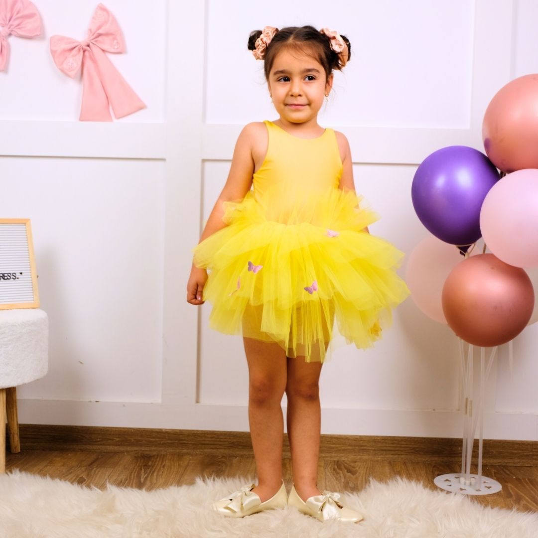 a little girl in a yellow dress standing in front of balloons