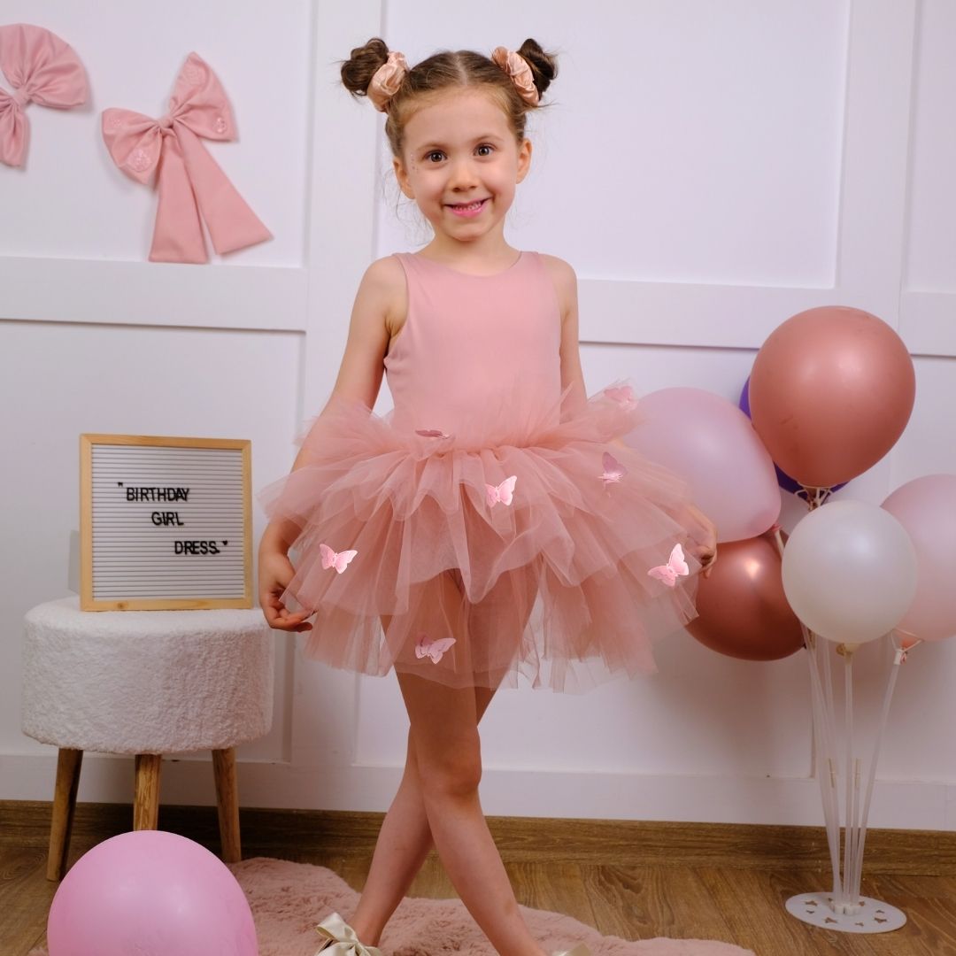 a little girl in a pink dress standing in front of balloons