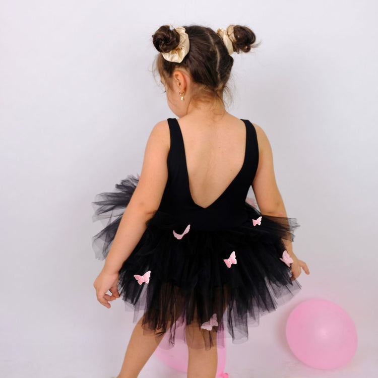 a little girl wearing a black dress and pink shoes