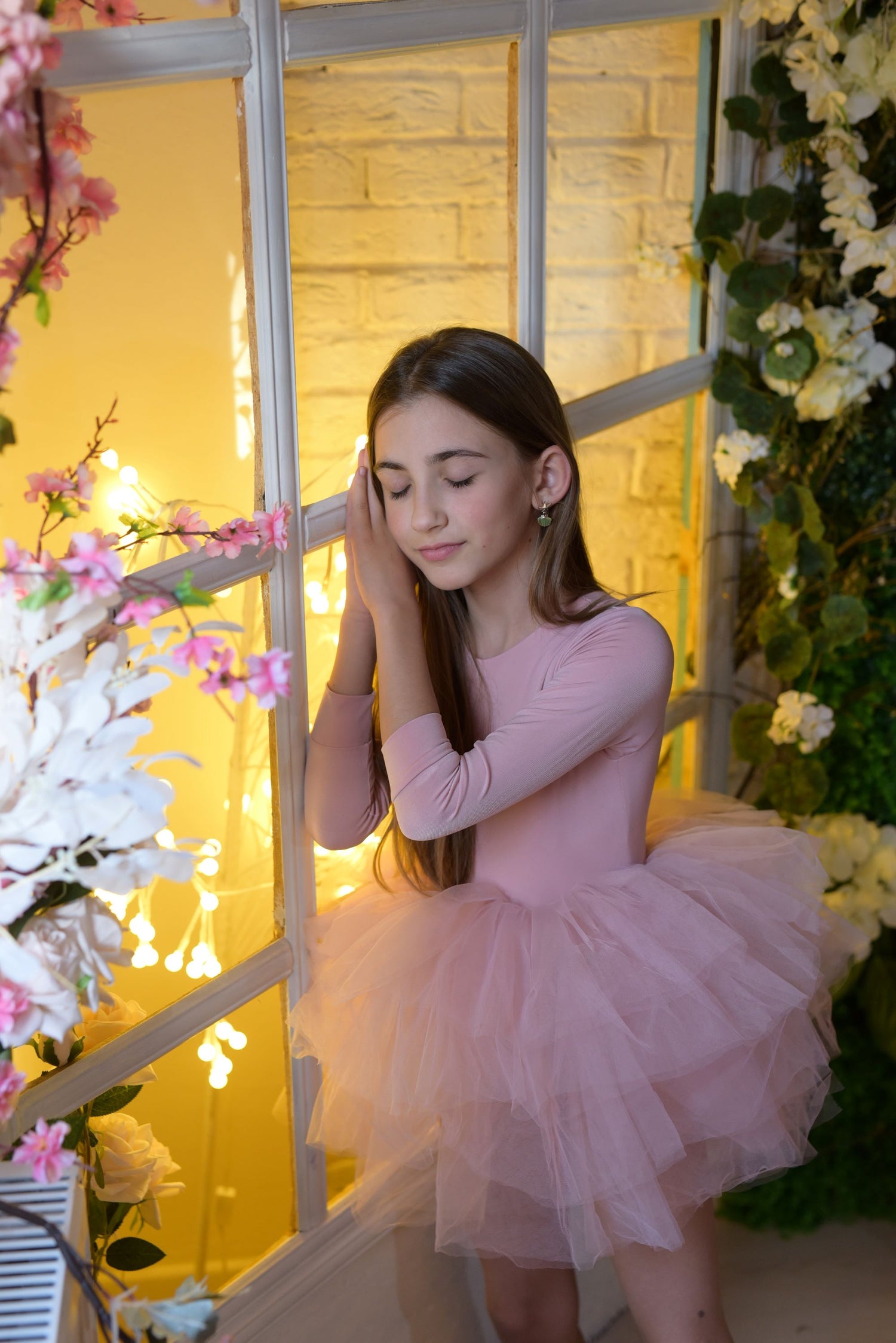 a young girl in a pink dress standing in front of a window