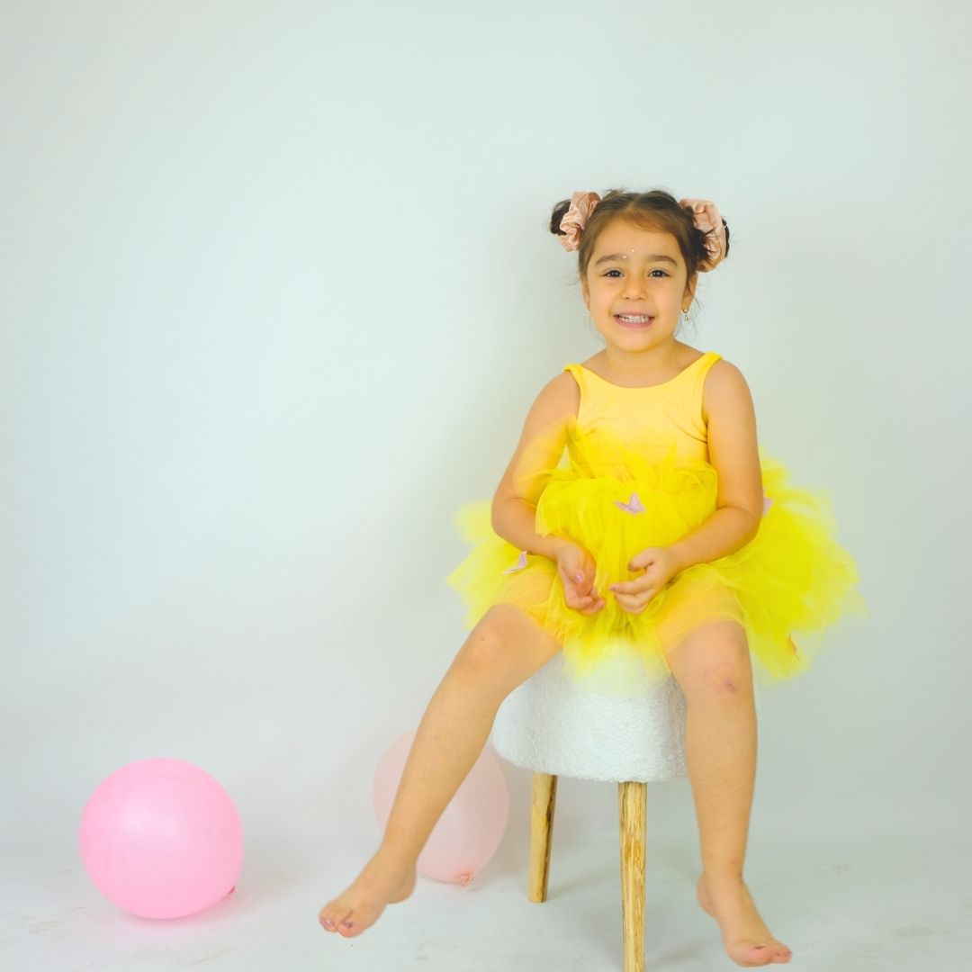 a little girl in a yellow dress sitting on a stool