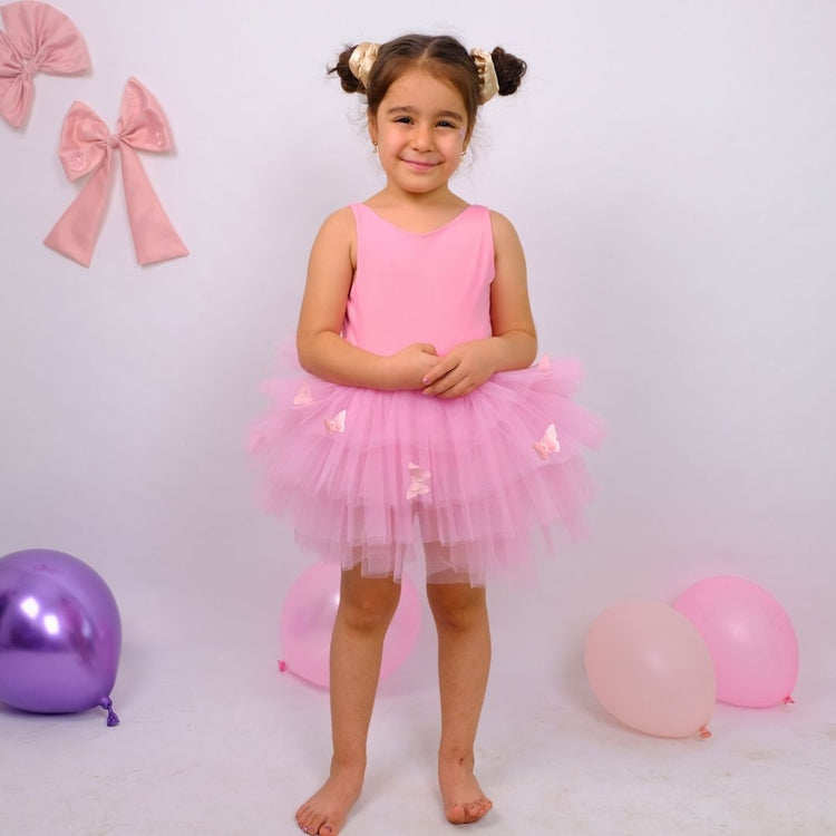 a little girl in a pink dress standing in front of balloons