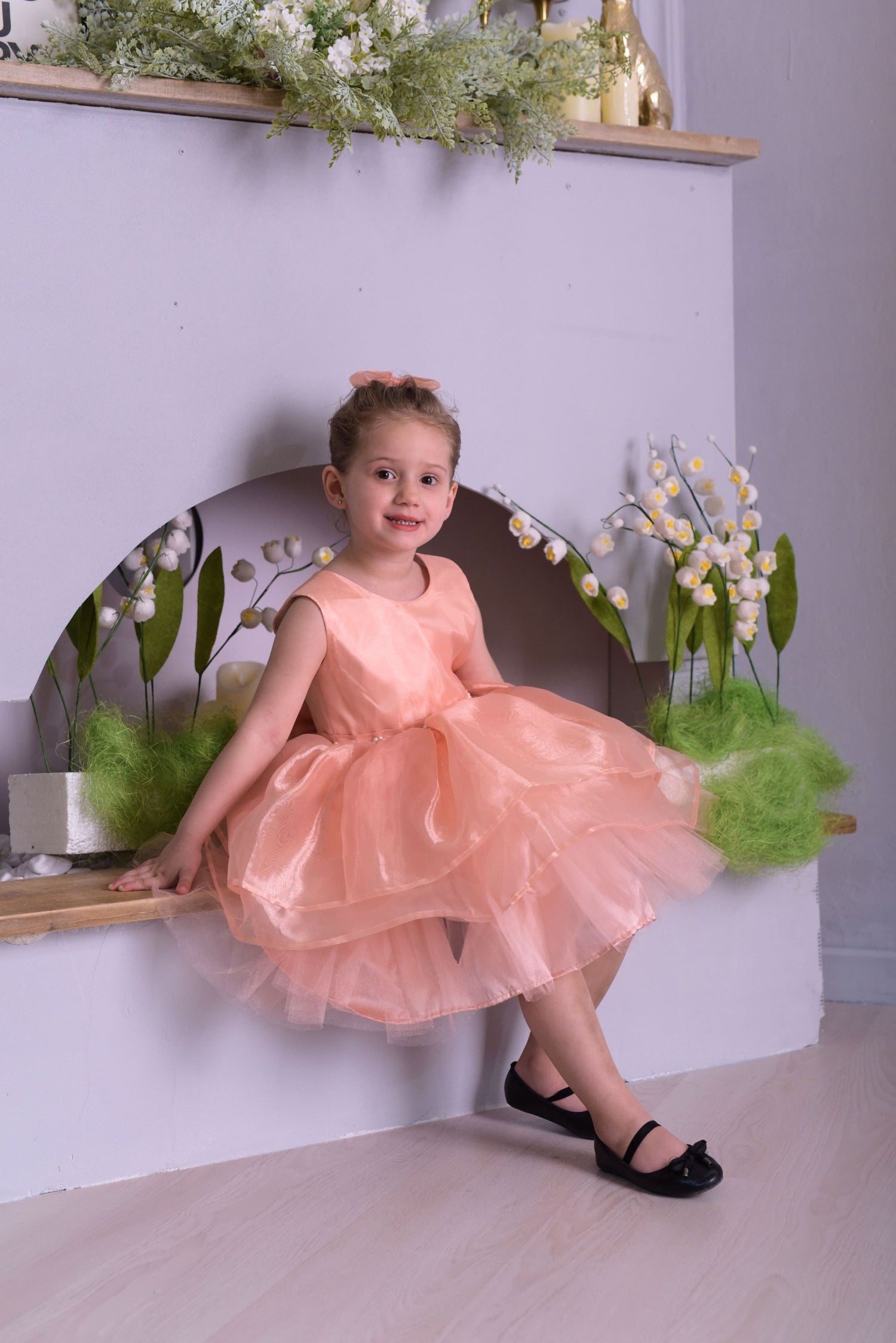 a little girl in a pink dress sitting on a shelf