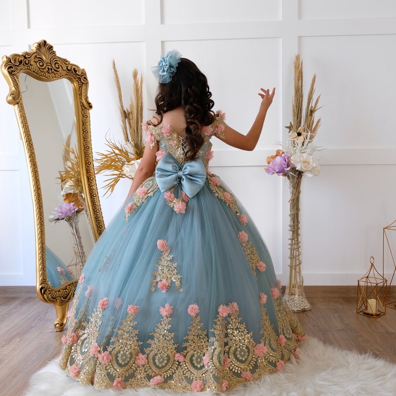 The bodice of the light pastel blue dress is laced and has laser flowers on it. The whole skirt is embroidered with lace and tulle on tulle.