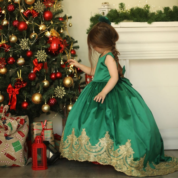 a little girl in a green dress standing next to a christmas tree