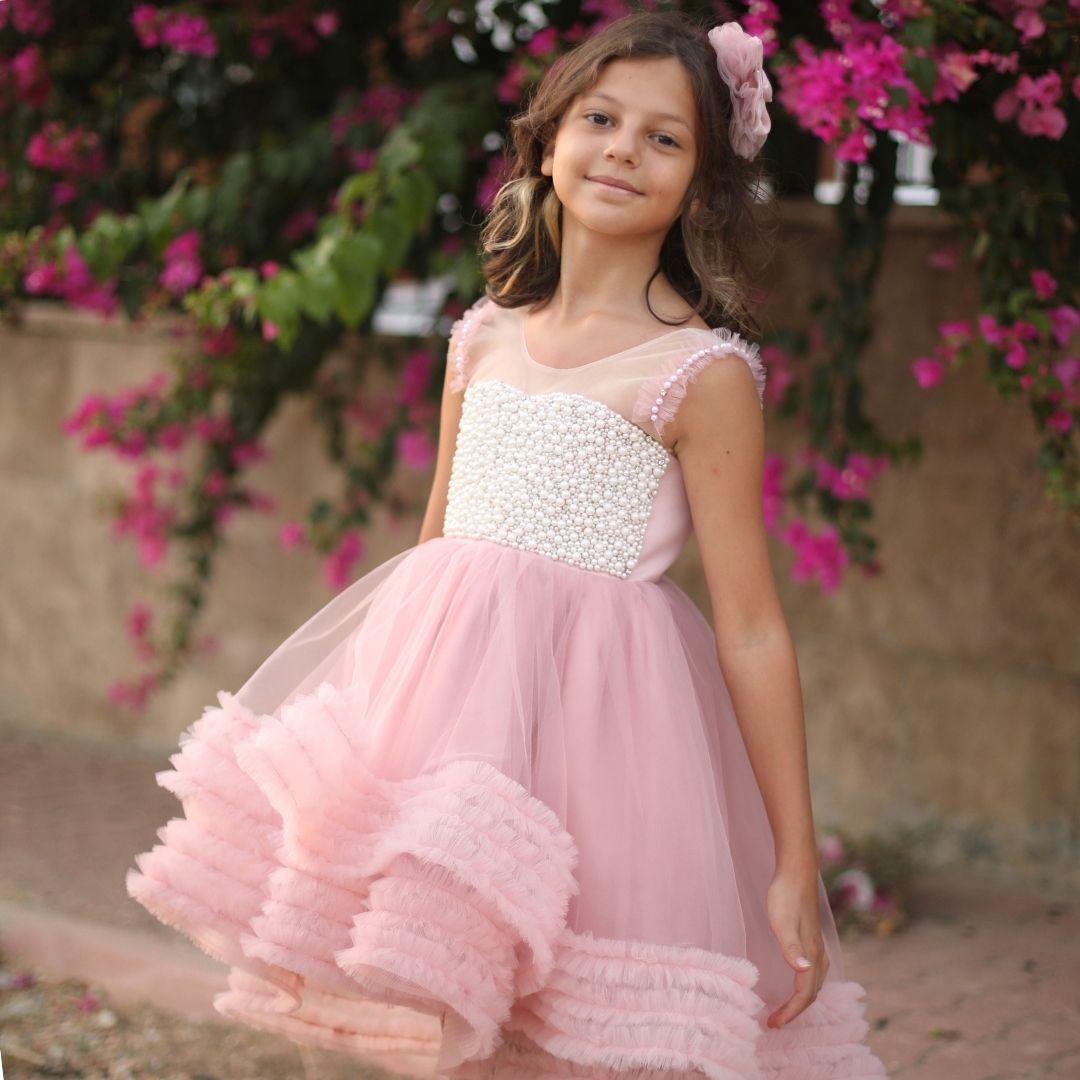 a little girl in a pink dress standing in front of flowers