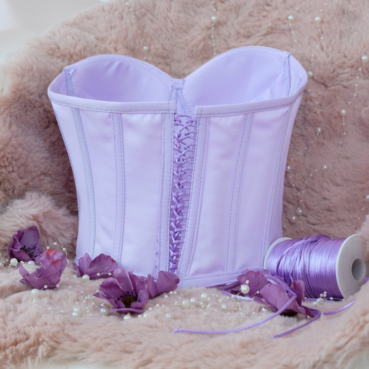 a purple corset sitting next to a spool of thread