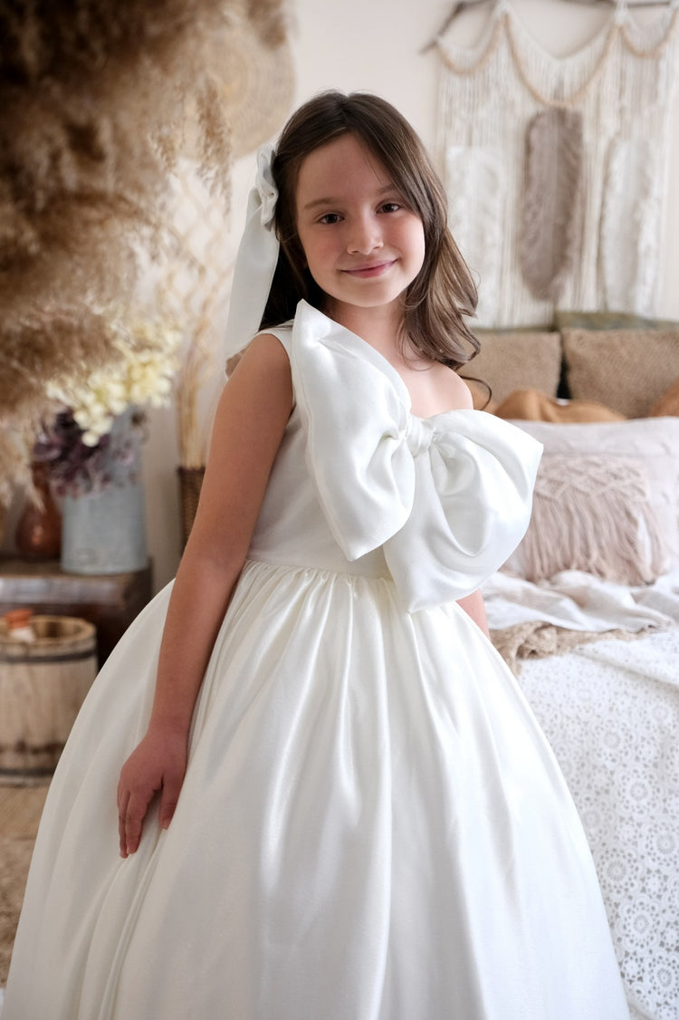 a little girl in a white dress standing in front of a bed