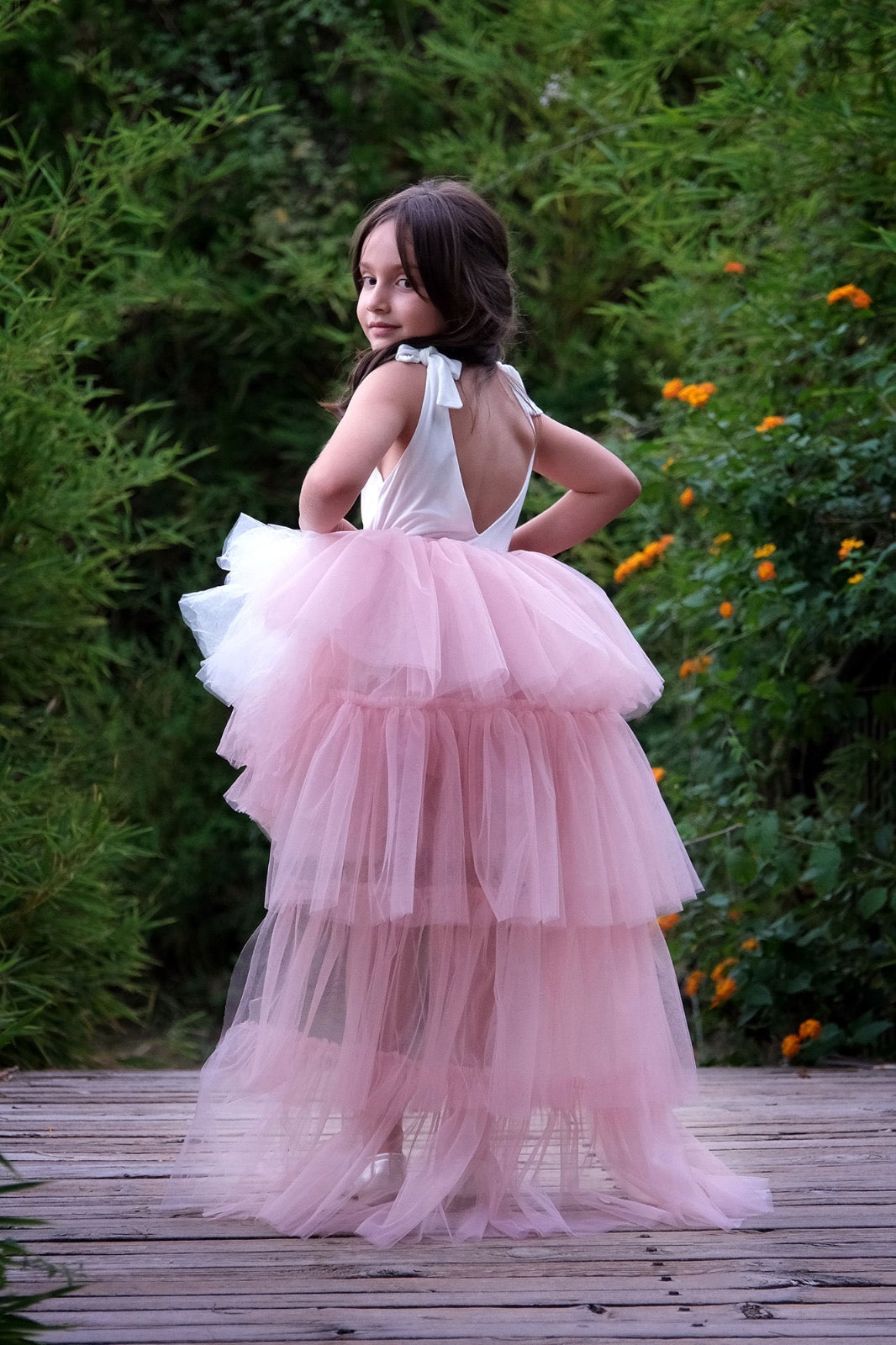 a little girl in a pink dress standing on a wooden walkway