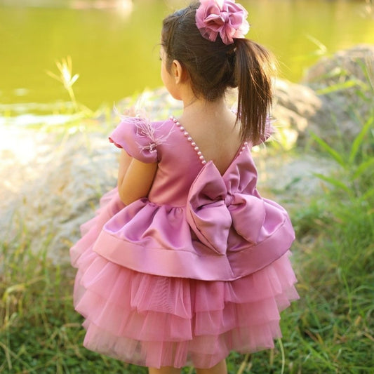 a little girl in a pink dress looking at the water