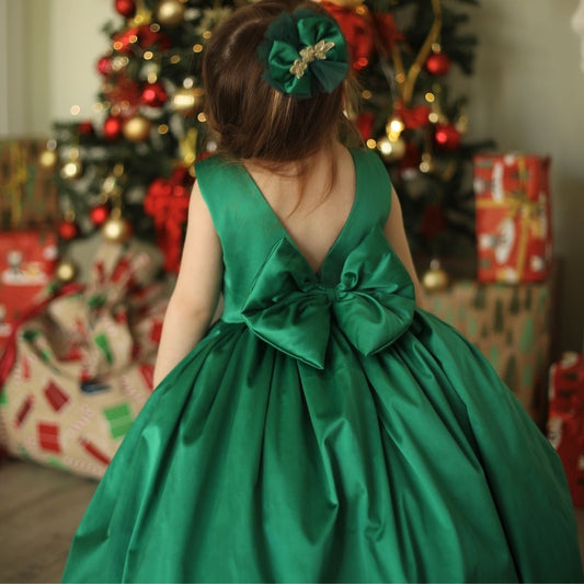 a little girl in a green dress standing in front of a christmas tree