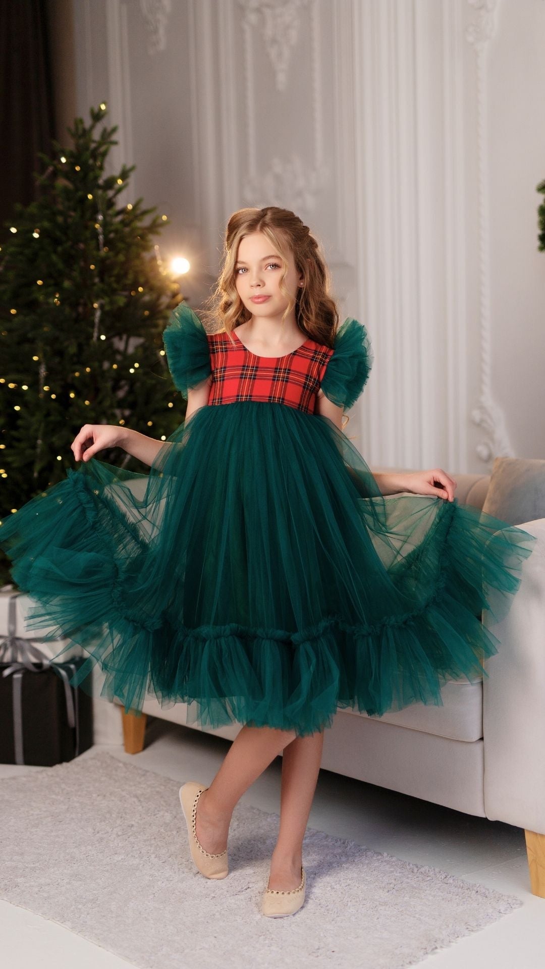 a little girl in a green dress standing in front of a christmas tree