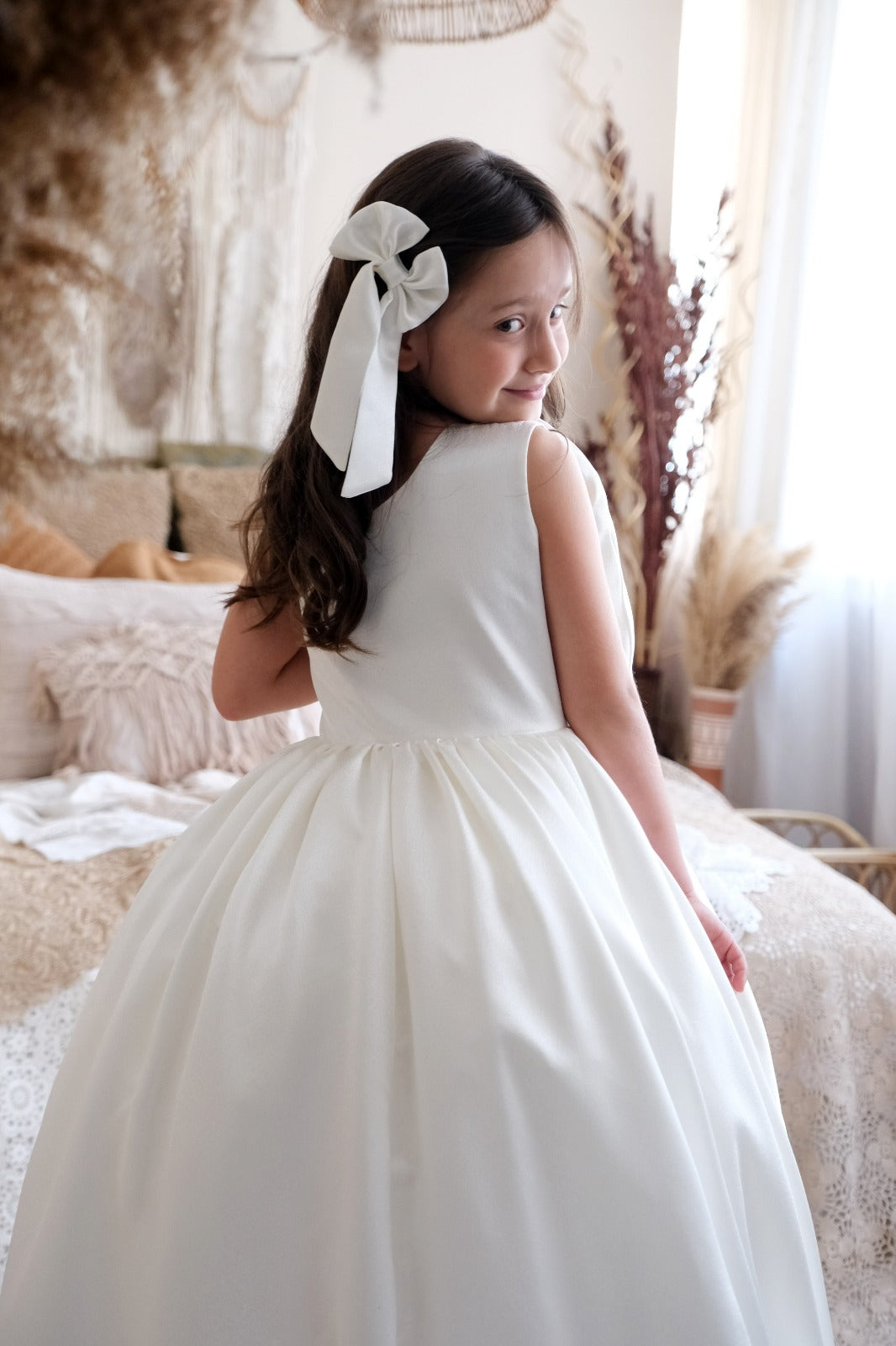 a little girl in a white dress standing on a bed