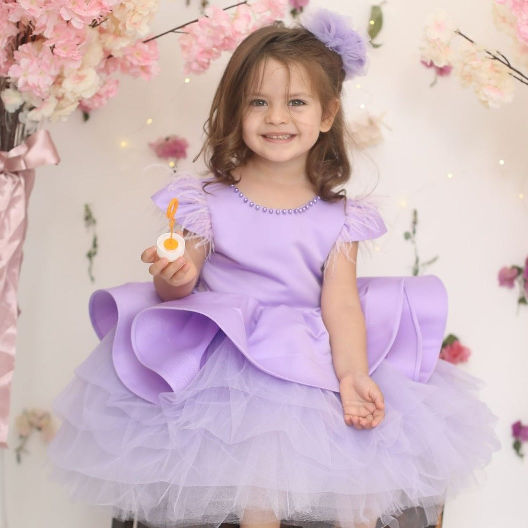 a little girl in a purple dress sitting on a stool