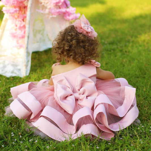 One shoulder blush pink girl’s dress featuring a stylish asymmetric design with a delicate ruffle trim, perfect for special occasions. The dress is made of soft, lightweight fabric, providing comfort and elegance for any young girl.