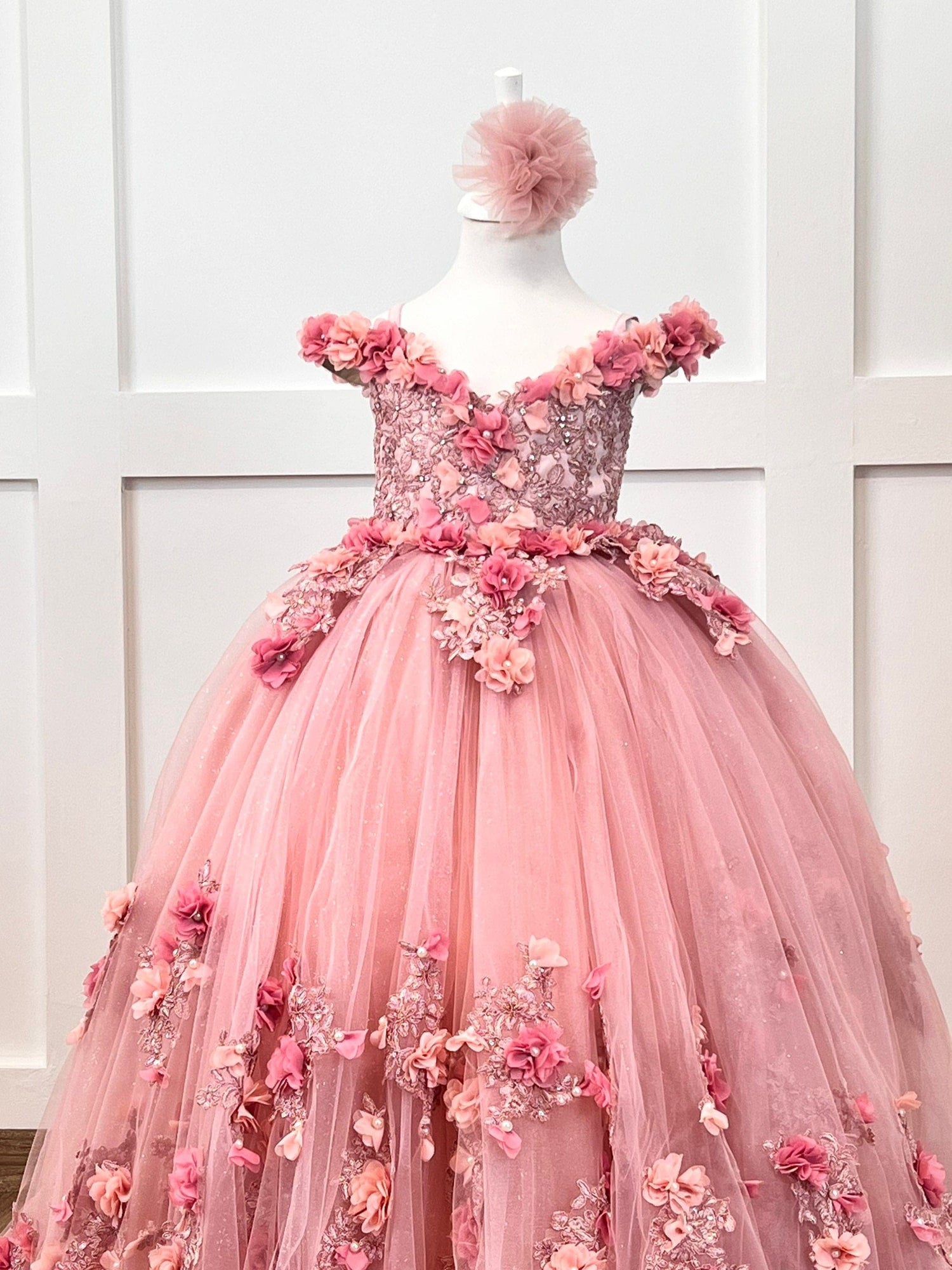 Quinceanera blush gown with satin bodice, lace, 3D colorful flowers, layered tulle skirt, and matching hair accessory.